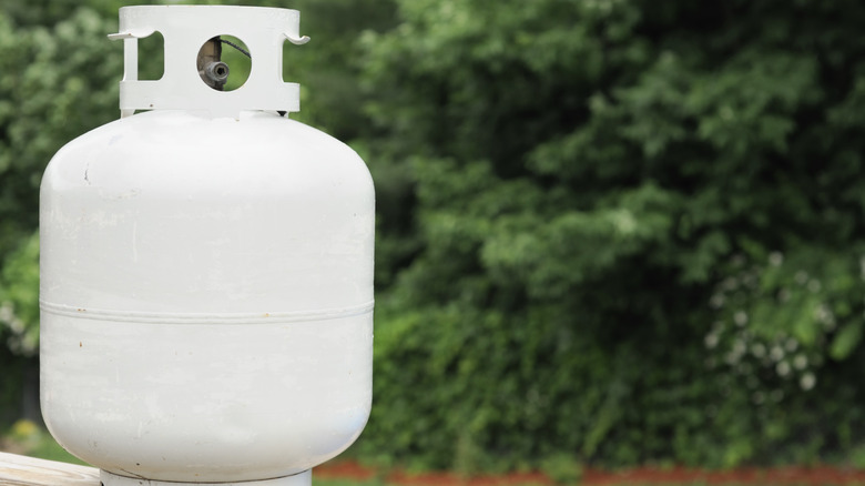 A propane tank in the sun on a deck with greenery in the background