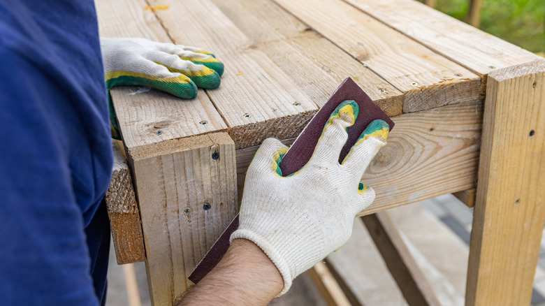 The person is sanding the edge of a wood structure.