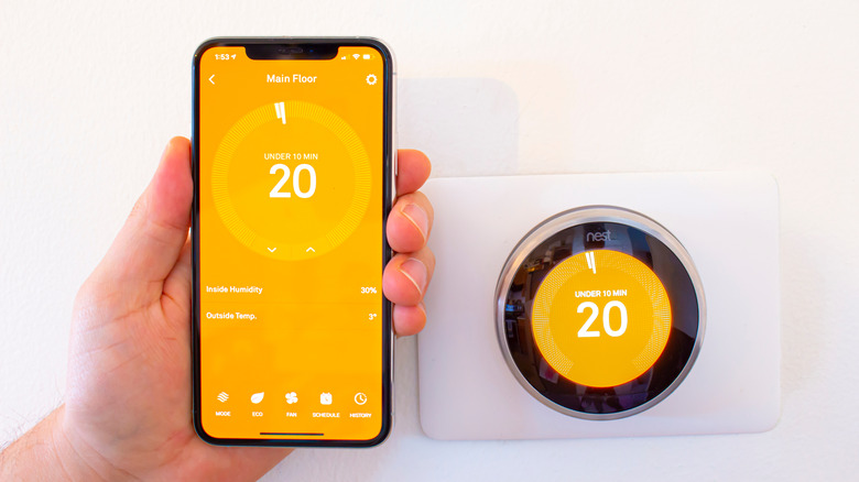 Hand holds a phone with the Nest app next to a Nest thermostat on a screen indicating HVAC running time