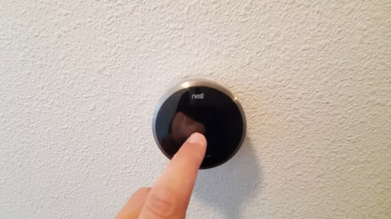 Finger touching a blank Nest thermostat screen mounted on the wall