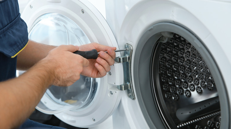 A man using a screwdriver on a washing machine