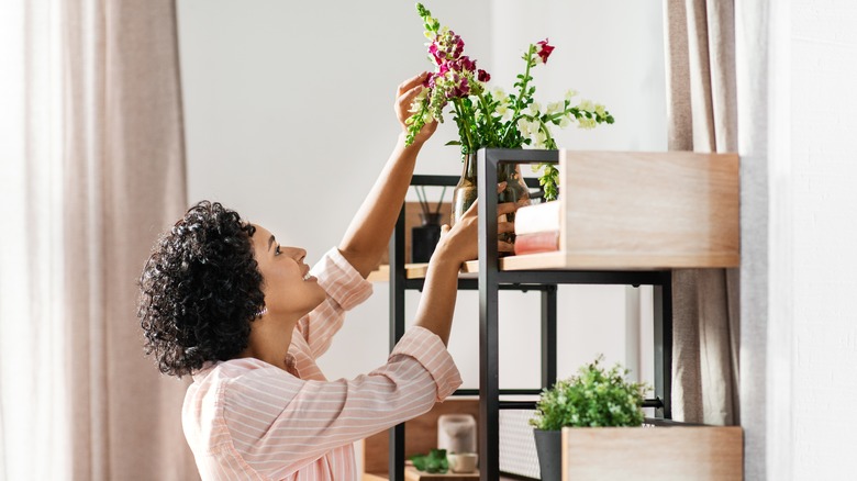 Woman placing flower vase on shelves in home