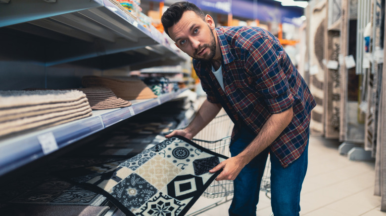 man choosing a doormat in a store