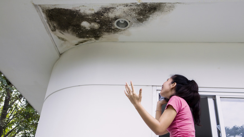 Agitated woman on a call annoyed by mold on the exterior ceiling in her home