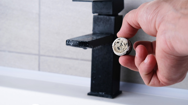 A person holding a faucet aerator with limescale