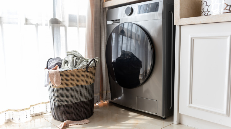 An overflowing laundry hamper sits next to a gray washing machine