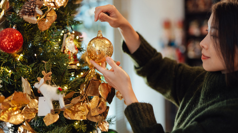 A woman decorating a Christmas tree with a golden ball ornament