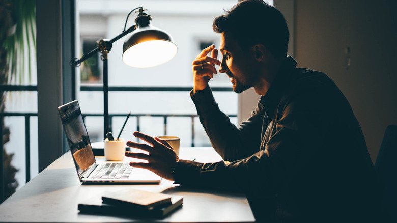 Man working on a laptop with a desk lamp on