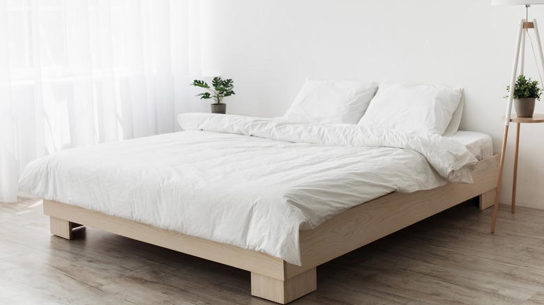 White bed with blanket and pillows on a wood bed frame in a white room