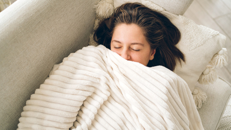 woman smiling under white blanket on couch