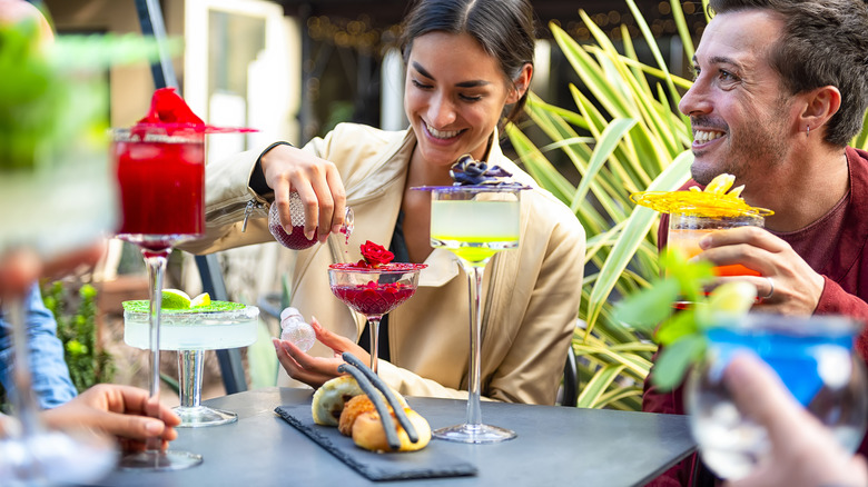 A group of people hanging out with cocktails around an outdoor bar table.