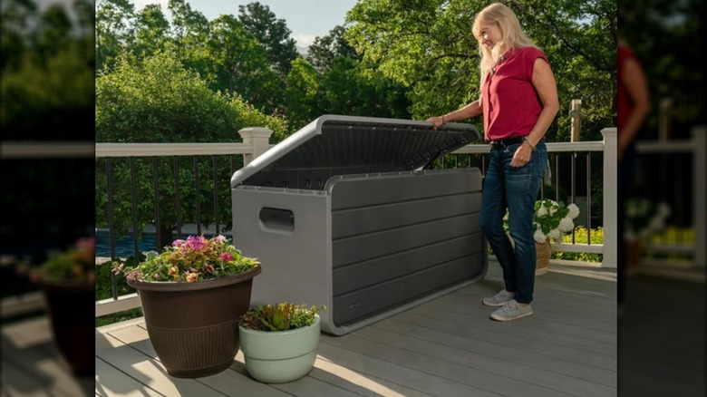 A smiling woman stores opens a large gray deck box on a patio