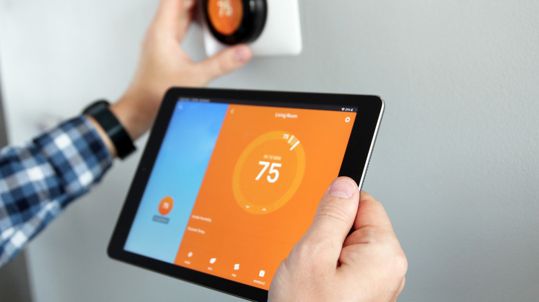 person adjusting smart thermostat while holding ipad with thermostat app on screen