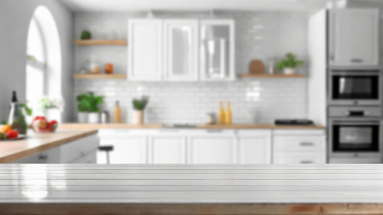 Blurred view of modern kitchen with white furniture with wooden table