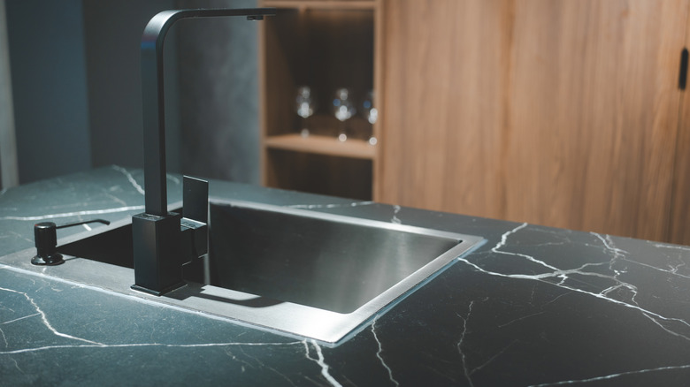 a sleek and modern kitchen sink and faucet set against a backdrop of dark cabinetry and a matte marble countertop