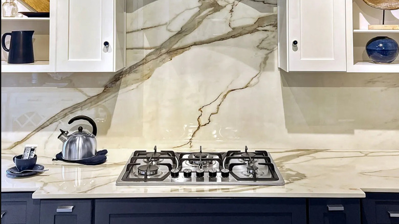 Kitchen with a porcelain countertop and backsplash featuring a marble pattern with black lower cabinets and white uppers