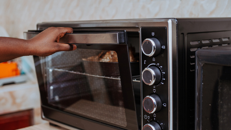 A hand opening a large countertop oven