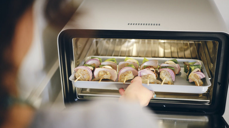 Person putting kebab skewers in a toaster oven