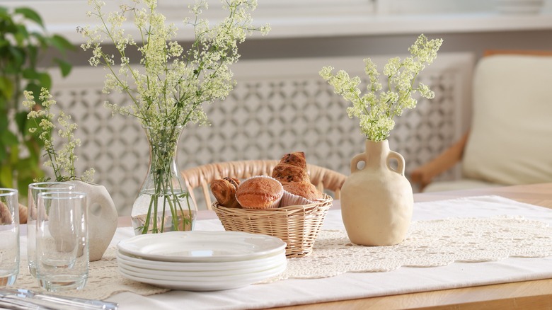 table set with stack of plates, glasses, basket of bread, and vases with baby's breath