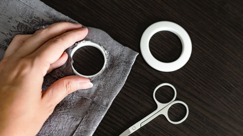 Person installing white eyelet in gray curtain