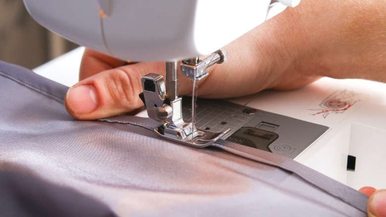 Person hemming gray curtain with sewing machine