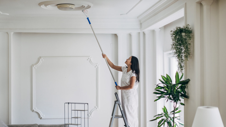 woman painting ceiling with primer with roller brush