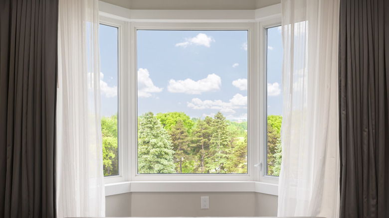 Bay window with drapes and net curtains and bright summer scene outside