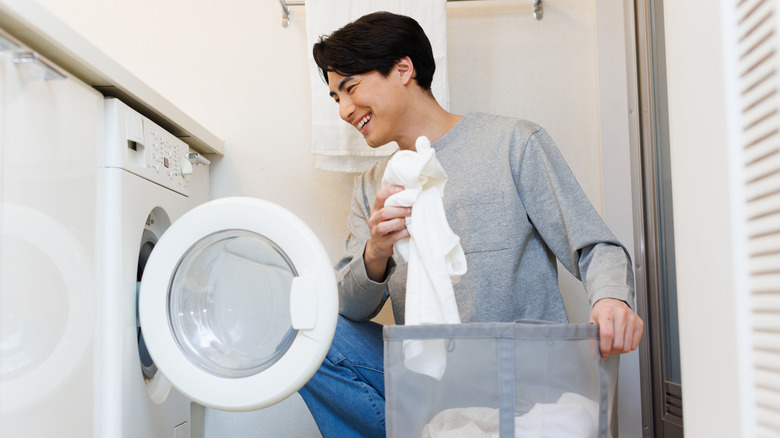 Man is taking clean laundry out of the dryer and placing it into a laundry bag