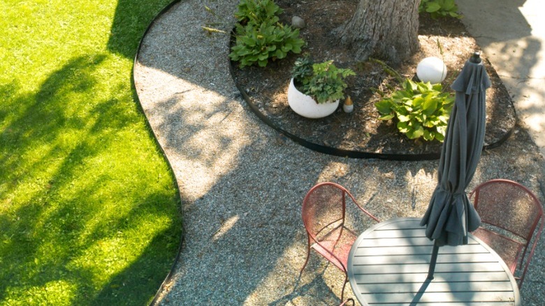 Two red metal chairs at outdoor dining table on gravel pad in backyard.