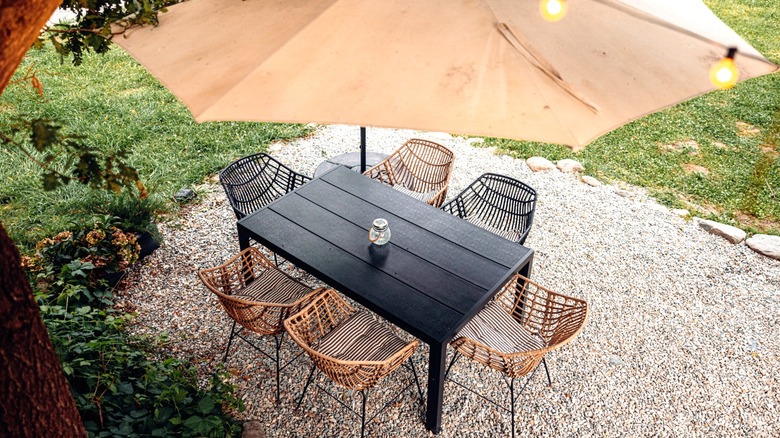 Six-seater outdoor dining set with umbrella on pea gravel pad in grassy lawn.