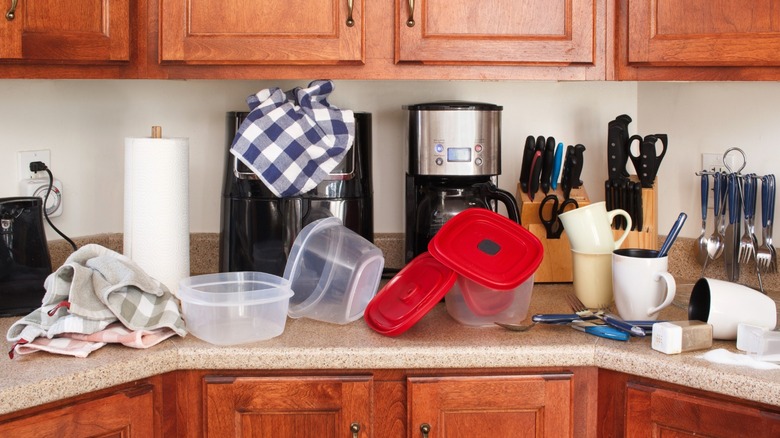 Kitchen countertop cluttered with storage containers, towels, cutlery, and coffee supplies