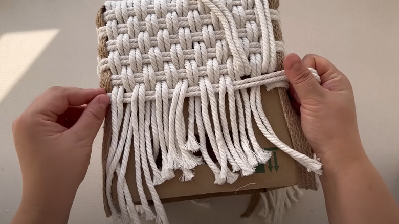 A woman transforming a cardboard box into a stylish woven storage container using rope.