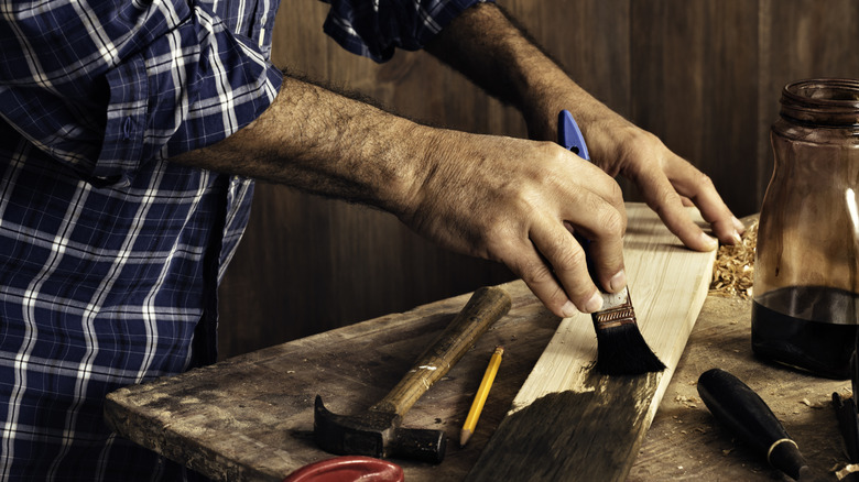 A person staining a wood board in a work shop