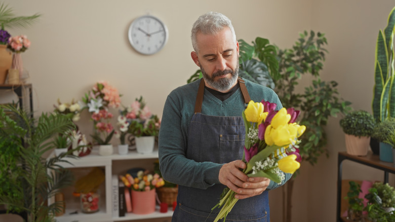 A bearded man with a bunch of tulips and the beginnings of a bouquet in his hands