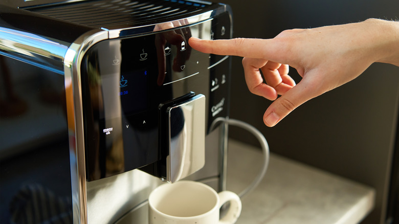 Hand pushing a button on a coffee maker with mug