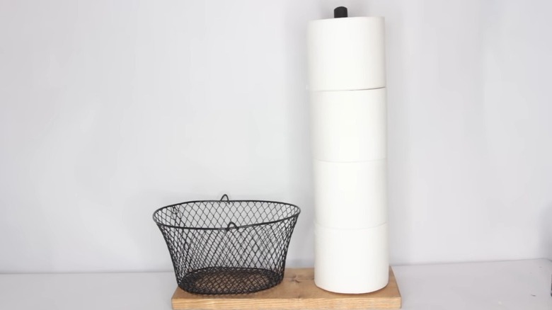 Black wire basket and toilet paper plunger handle on wood plank