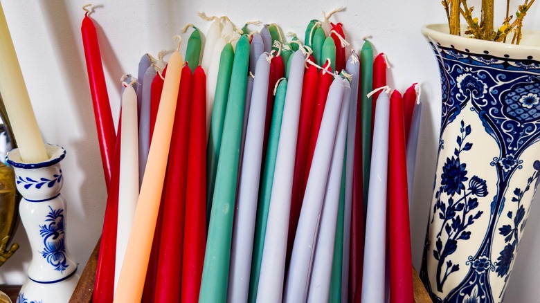 Pile of colorful taper candles in wooden tray