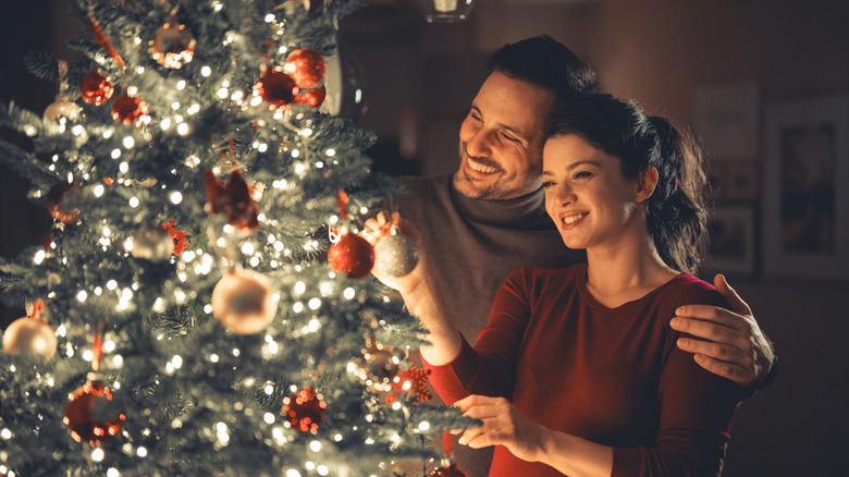 A couple hanging up Christmas tree ornaments