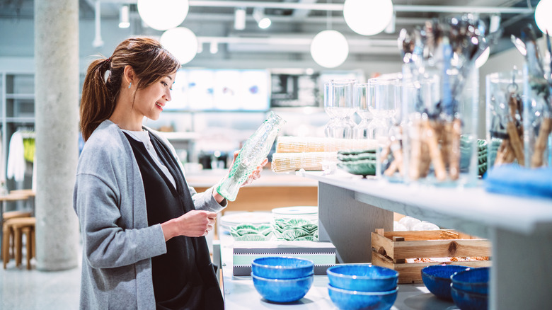 Woman looking at a tall glass vase in a store.