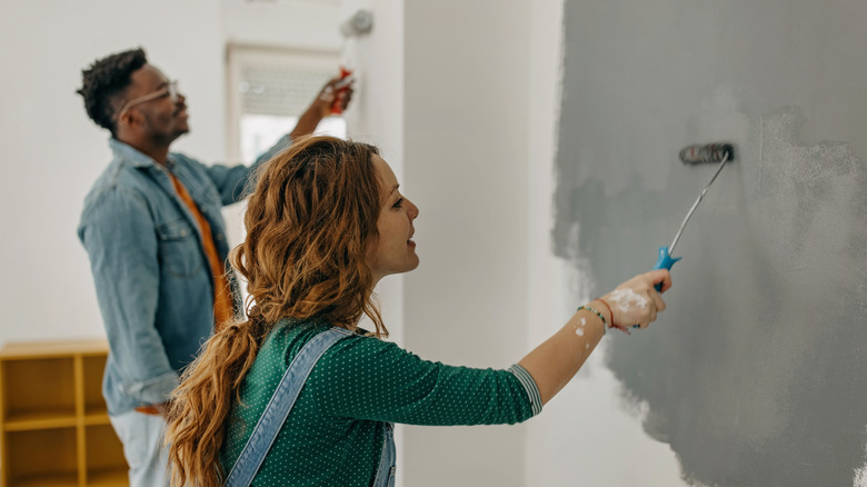 A couple painting a wall in gray.