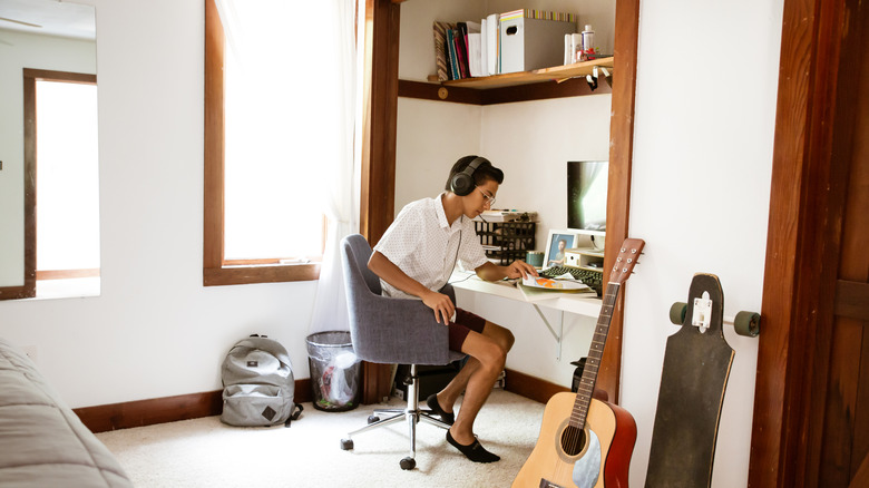 Boy sitting in his closet converted into a workspace with guitar in forefront.