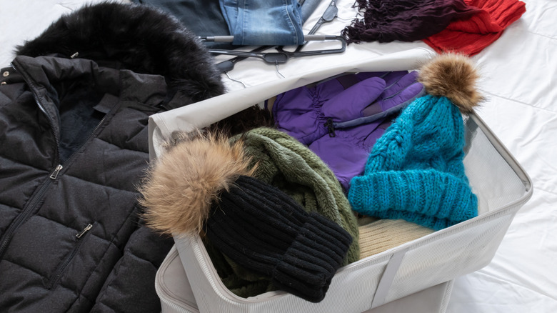 Fabric box of winter accessories including gloves and hats on a white bed