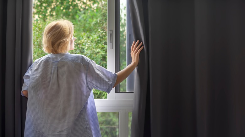 woman opening blackout curtains on window