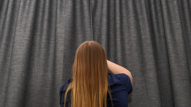 Woman closing gray curtains on walll