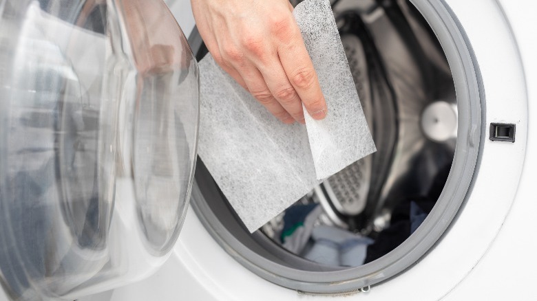 Person tossing dryer sheet in dryer