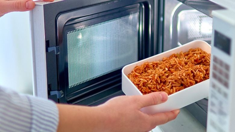 Person putting uncovered food in microwave