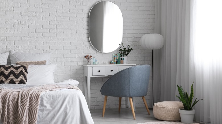 A white vanity table and gray chair with mirror in a bedroom