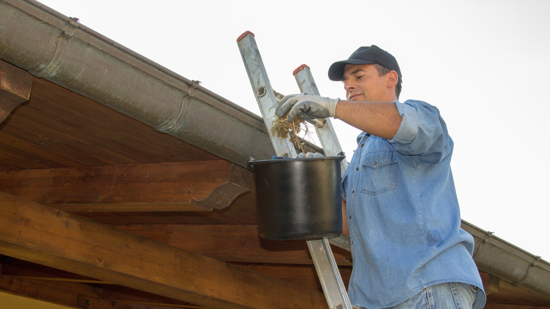 Man holding a bucket and cleaning debris out of a gutter