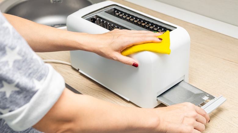 closeup of woman wiping a white toaster with a yellow cloth