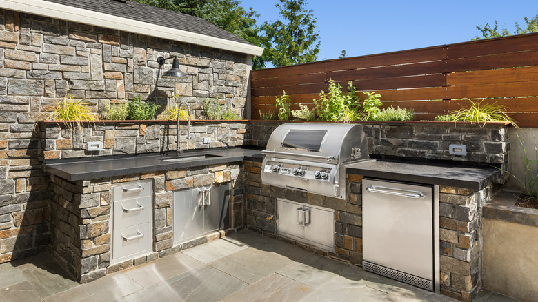 An outdoor kitchen has a sink, grill, and under-counter fridge.